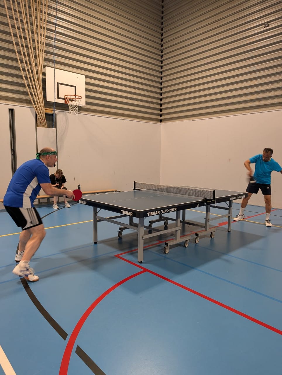 A member in blue leaning in with his forehand against an opponent in the hall