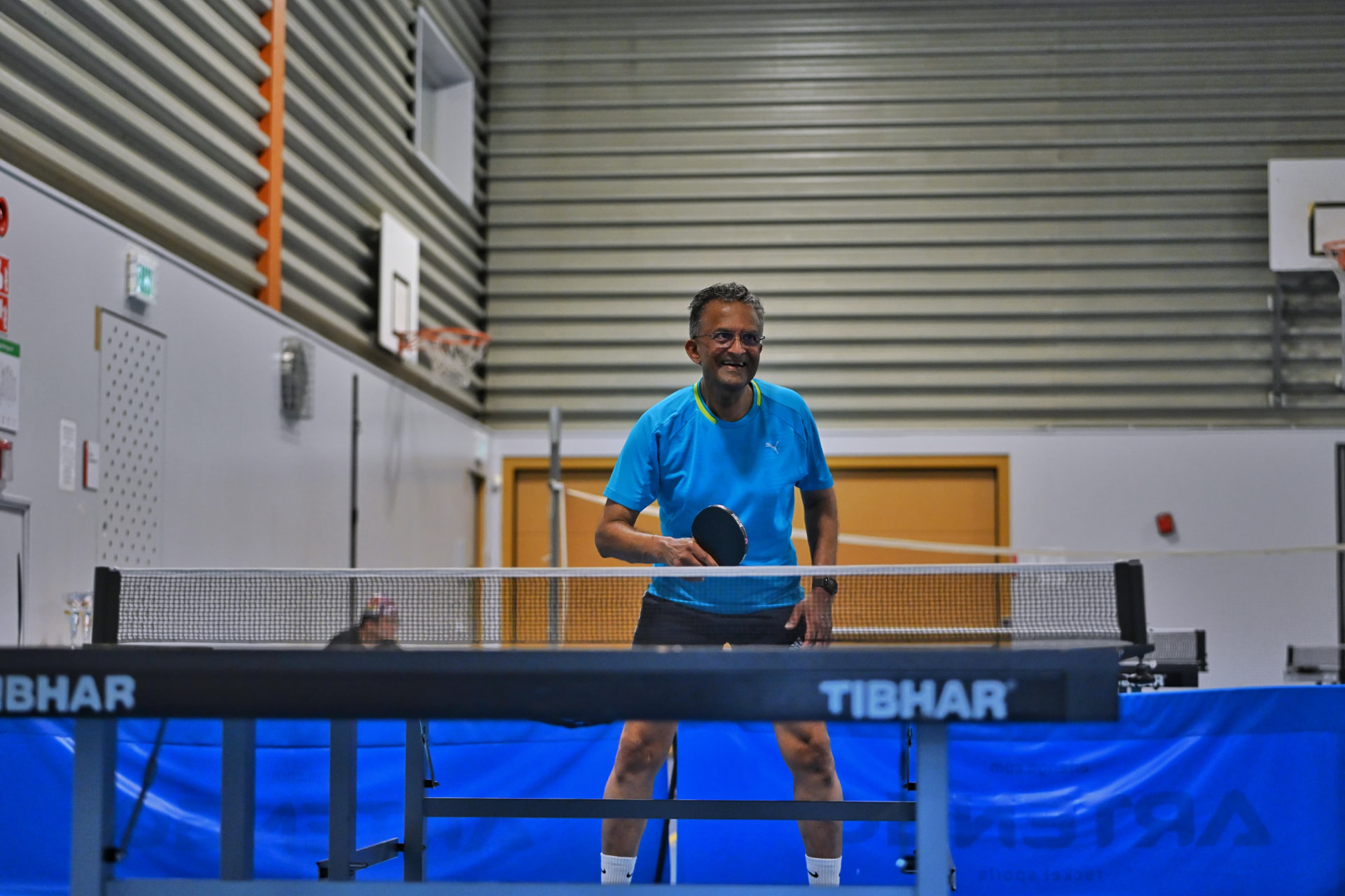 A smiling member waiting to return a serve during an open evening