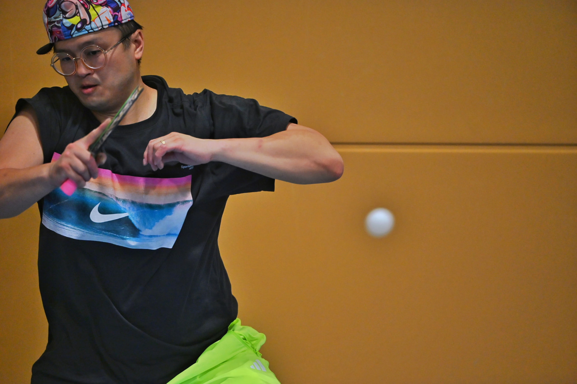 A member in a cap and glasses keeping his eye on the ball mid-rally
